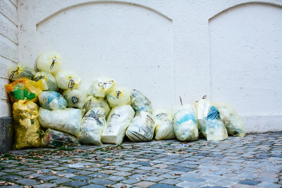 The image depicts the exterior corner of a building with weathered green wooden cladding, positioned on a street in an urban environment. Several black plastic rubbish bags are piled against the build